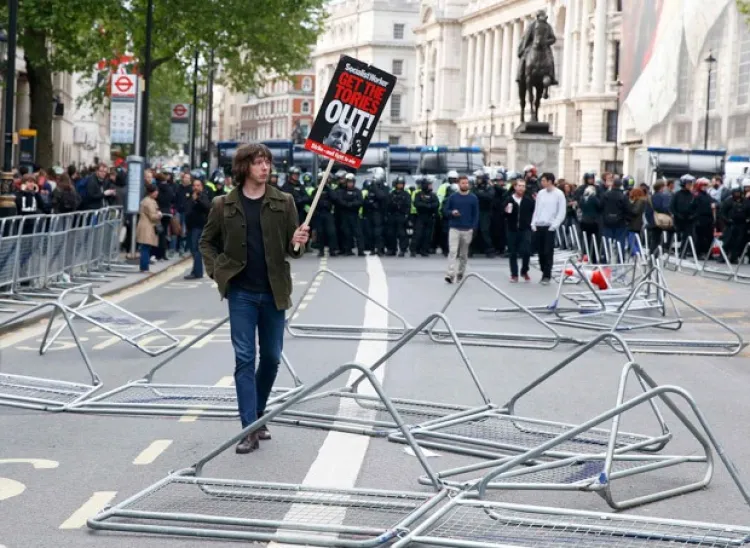 Manifestante segura um cartaz próximo a barreiras de retenção na Downing Street, em Londres, durante protesto contra o Partido Conservador (Foto: Phil Noble/Reuters)
